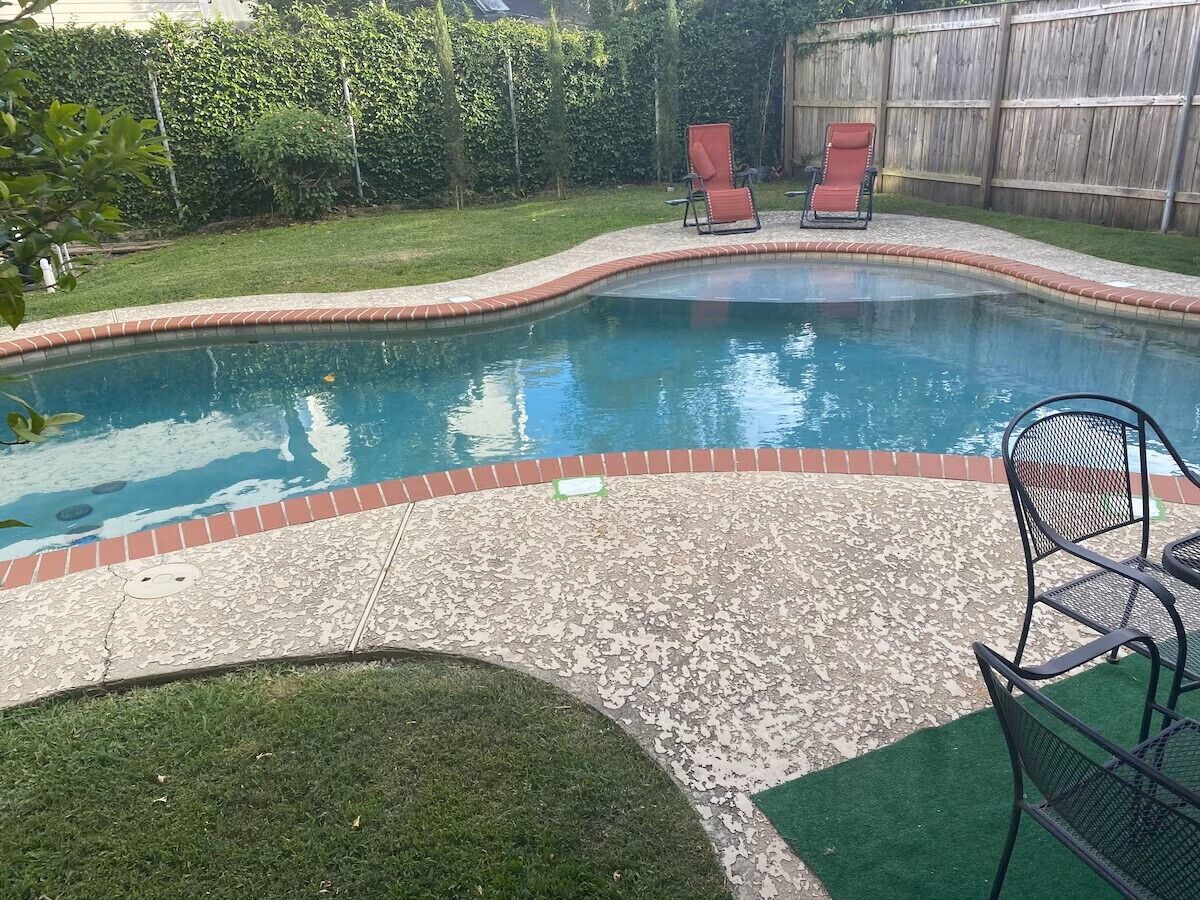 A swimming pool with a brick edge, two red chairs, and a green artificial turf area.