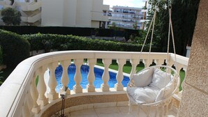 A white outdoor seating area with a hanging chair, a small rock planter, and a view of a swimming pool.