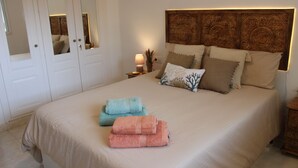 A neatly made bed with a headboard, a nightstand with a lamp, and a mirror on the wall.