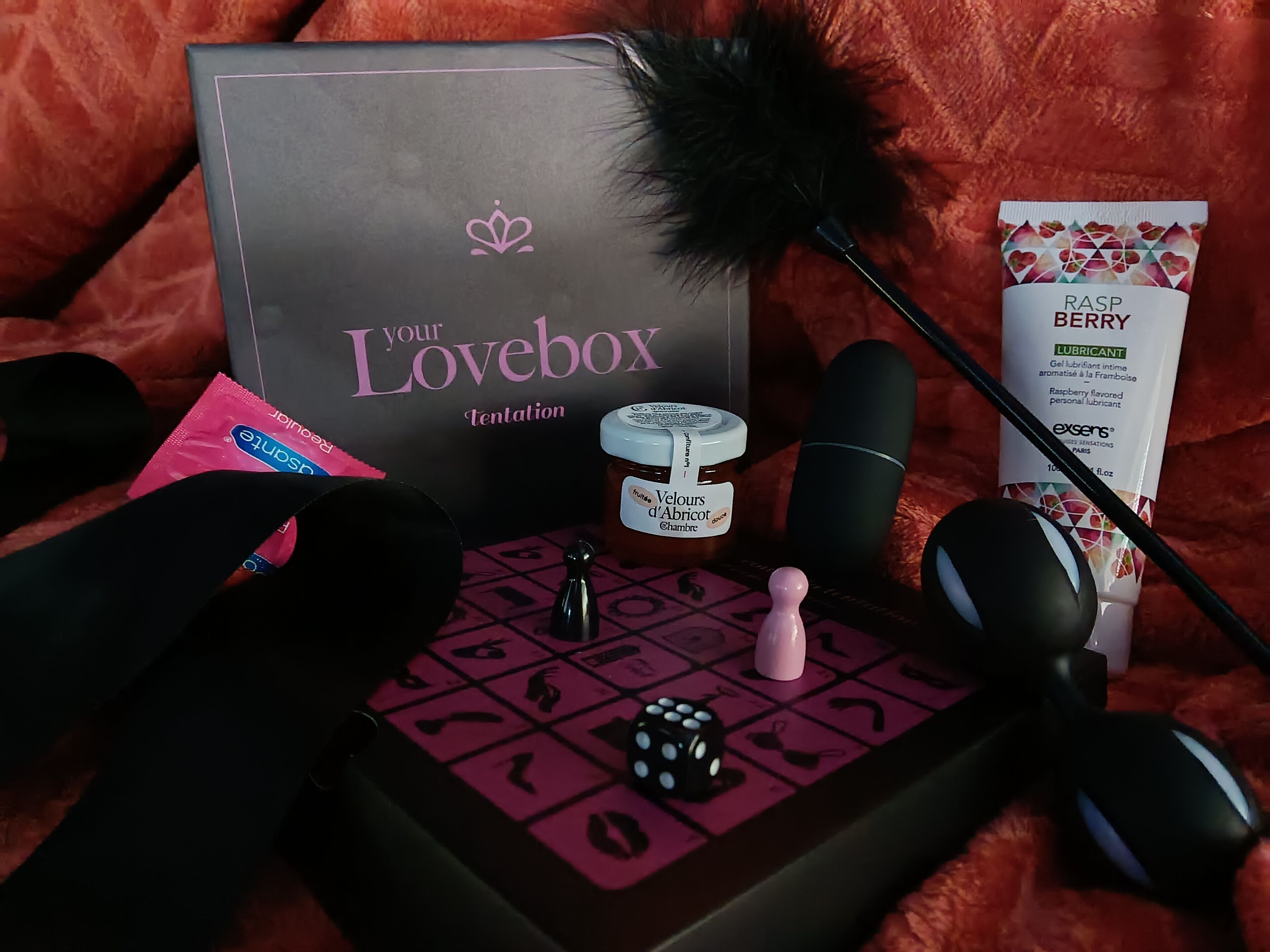 A box labeled "Lovebox Tentation" with a jar of honey and a box of RASP Berry lubricant.