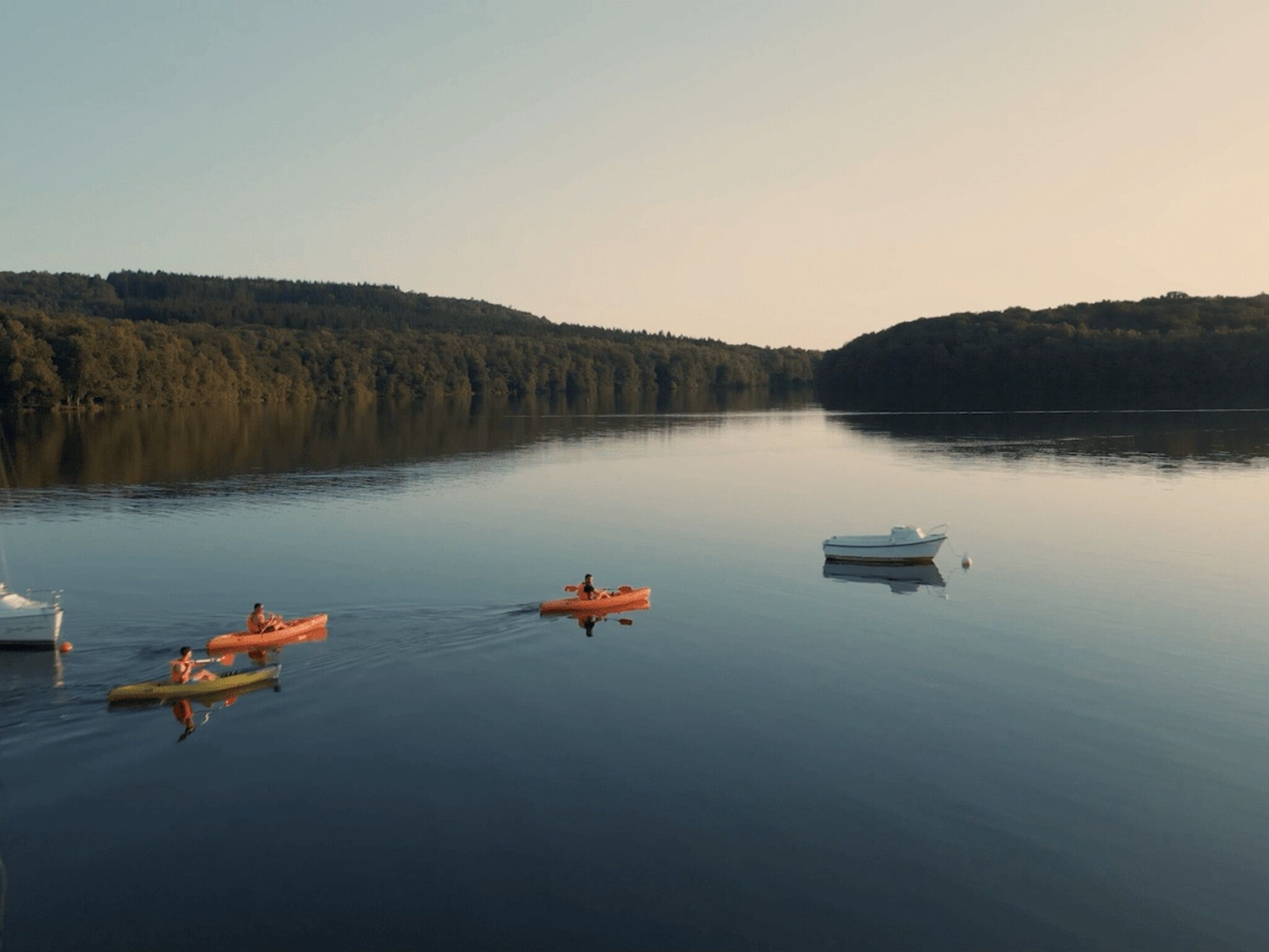 Un lago tranquilo con barcos y una orilla bordeada de bosque.