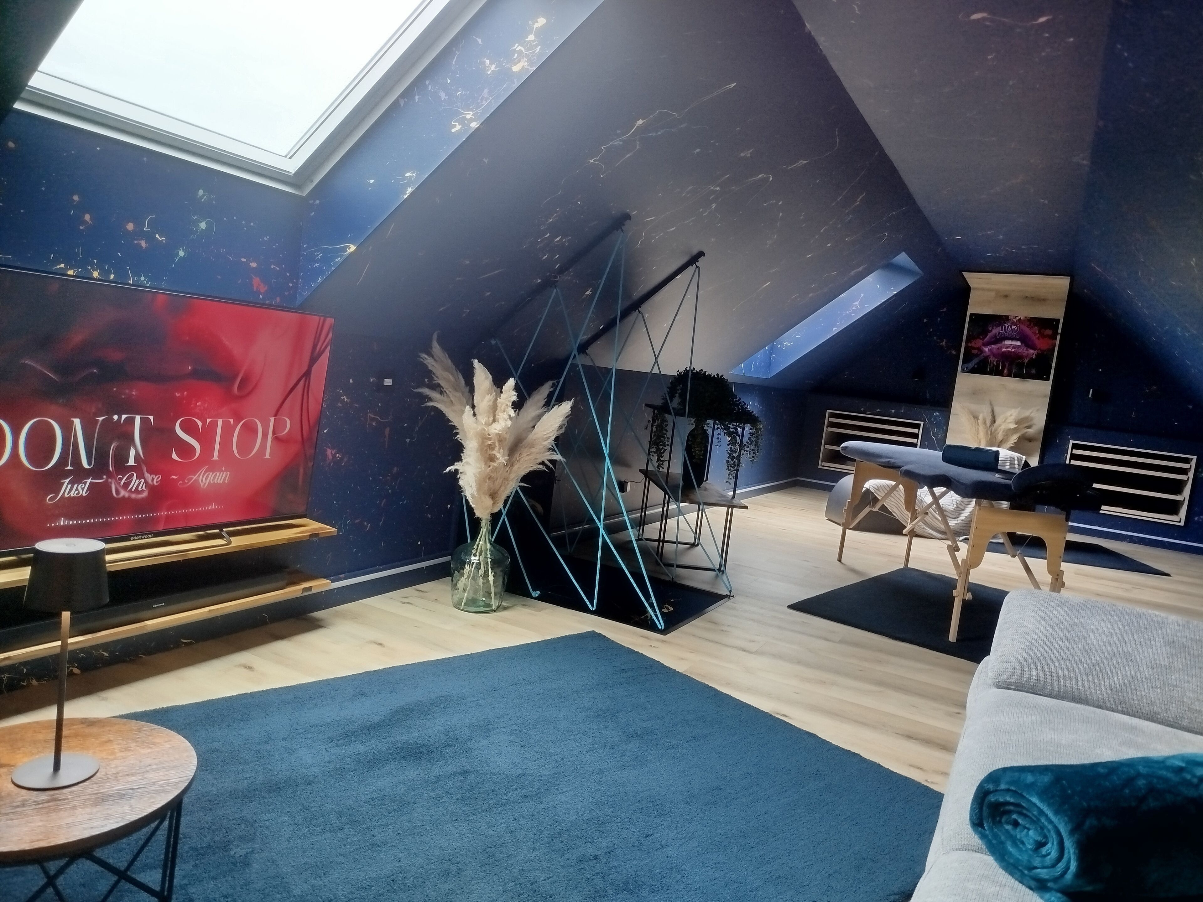 Ett modernt rum i loftstil med ett sluttande tak, en stor affisch, en sittgrupp med en soffa och stolar samt ett litet runt bord.