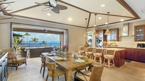 A spacious kitchen with a large island, wooden chairs, and a view of the ocean. - Blue Lani at Holua Kai (Kailua-Kona)