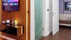 Una sala de estar moderna con un televisor de pantalla plana montado en una pared de madera, un ventanal de vidrio y una zona de estar con sofá y estante para la televisión.