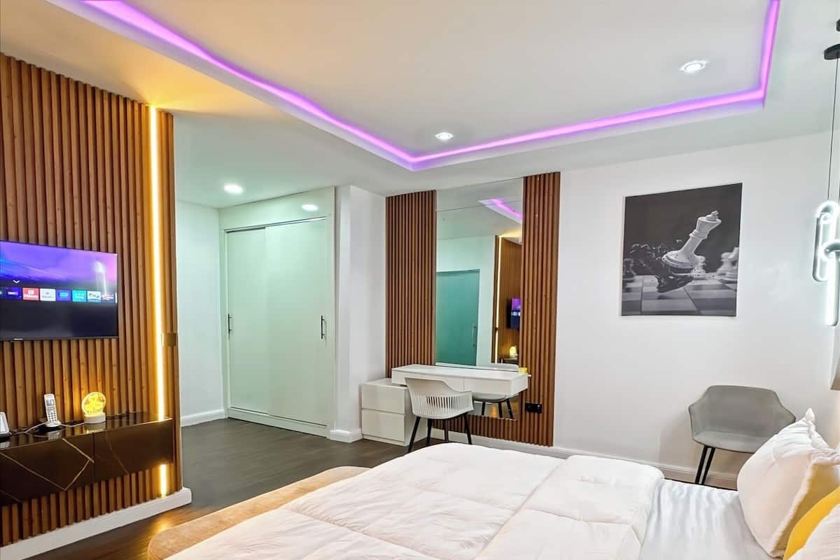 A modern bedroom with a large bed, a desk, a chair, and a TV mounted on the wall.