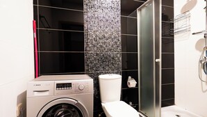 Kompakti kylpyhuone, jossa on pesukone, wc ja lasiseinällä erotettu suihkutila.