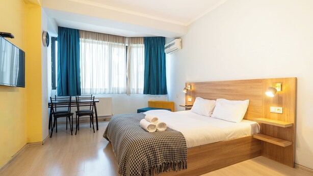 Hotellihuone, jossa on puinen sänky, työpöytä tuoleineen, televisio ja ikkuna, jossa on verhot.