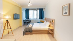Hotellihuone, jossa on sänky, yöpöytä, lamppu ja suuret ikkunat, joista on näkymä ulos.