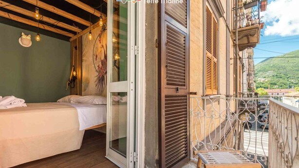 Een kamer met een bed, een balkon met een metalen hekwerk en een deur die naar buiten leidt.
