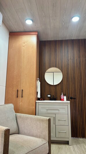Ein Zimmer mit einem Holzschrank, einem runden Spiegel, einem weißen Waschbecken und einem beigen Sofa.