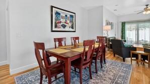 A dining area with a wooden table and chairs, a framed artwork on the wall, and a view of the living room through a window. - Cozy Spacious New Build • 10 minutes to Beaches (Largo)