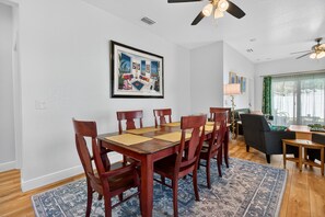 A dining area with a wooden table and chairs, a framed artwork on the wall, and a view of the living room through a window. - Cozy Spacious New Build • 10 minutes to Beaches (Largo)