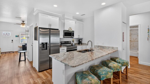 A modern kitchen with white cabinets, stainless steel appliances, a marble island, and a seating area with patterned stools. - Cozy Spacious New Build • 10 minutes to Beaches (Largo)