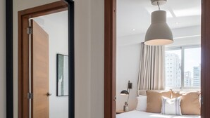 Habitación de hotel con una cama grande, una mesita de noche, una lámpara y vistas a la ciudad a través de una ventana.