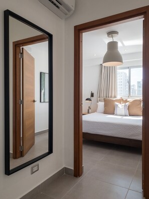 Ein Hotelzimmer mit einem großen Bett, einem Nachttisch, einer Lampe und Blick auf die Stadt durch ein Fenster.