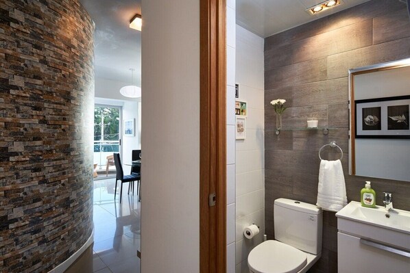 A modern bathroom with a brick accent wall, a white toilet, a glass shower enclosure, and a white sink with a mirror above it.