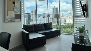 A modern living room with a black leather sofa, a floor lamp, and a city view through large windows. - *Classy*wifi-A/C-Gym-BlueMall-YellowKey (Santo Domingo)