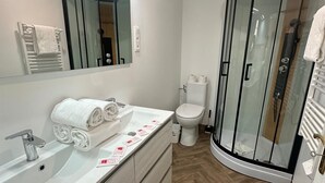 Un baño moderno con cabina de ducha de vidrio, un lavabo blanco con espejo y un inodoro.