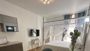 Habitación de hotel pequeña con cama, escritorio, silla, televisor, microondas y lavamanos.