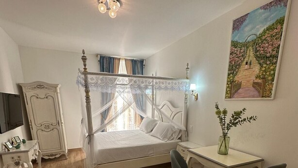 Un dormitorio con cama con dosel, un escritorio con sillas, un televisor y un cuadro en la pared.