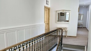 Una escalera con barandillas ornamentadas en negro y dorado, una barandilla de madera y una pared de color claro con una puerta y un espejo.