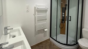 Un baño moderno con ducha en esquina, un lavamanos blanco con espejo y un inodoro.