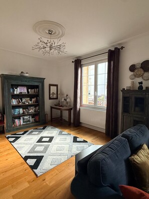 A living room with a sofa, a patterned rug, a bookshelf, a small table with a lamp, and a window with curtains. - 7-ROOM VILLA, 15 MINUTES BY BUS OR 30 MINUTES ON FOOT TO THE PARCOURS DU PAPE   (Montigny-lès-Metz)