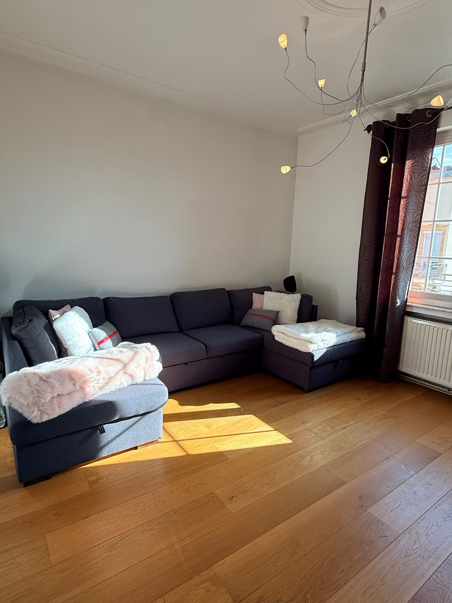 A modern living room with a dark-colored sofa, a small ottoman, and a fluffy throw blanket.