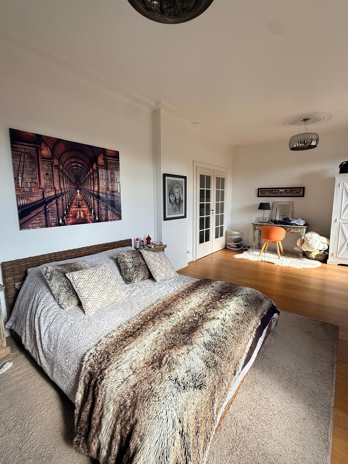 Een slaapkamer met een groot bed, een schilderij, een deur en een kleine tafel met spullen erop.