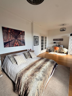 Makuuhuone, jossa on suuri sänky, taulu, ovi ja pieni pöytä, jonka päällä on tavaroita.