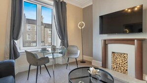 Un salon moderne avec une cheminée, un téléviseur à écran plat fixé au-dessus, une table basse ronde en verre, un canapé et une table à manger avec des chaises.