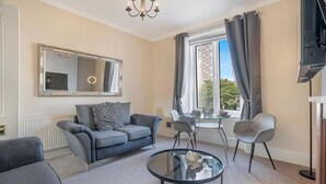 Un salon moderne avec un canapé, des fauteuils, une table basse en verre et un téléviseur.