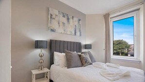 A bedroom with a bed, two bedside tables, a window, and a painting on the wall. - Holburn Lodge by Duthie Park Work Ready Fast Wi-fi (Aberdeen)