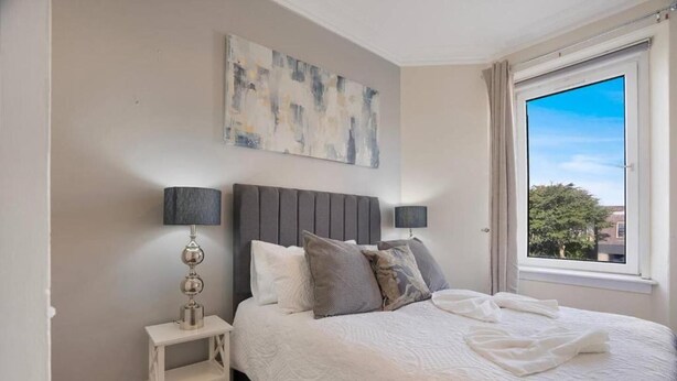 Une chambre à coucher avec un lit, deux tables de chevet, une fenêtre et un tableau au mur.