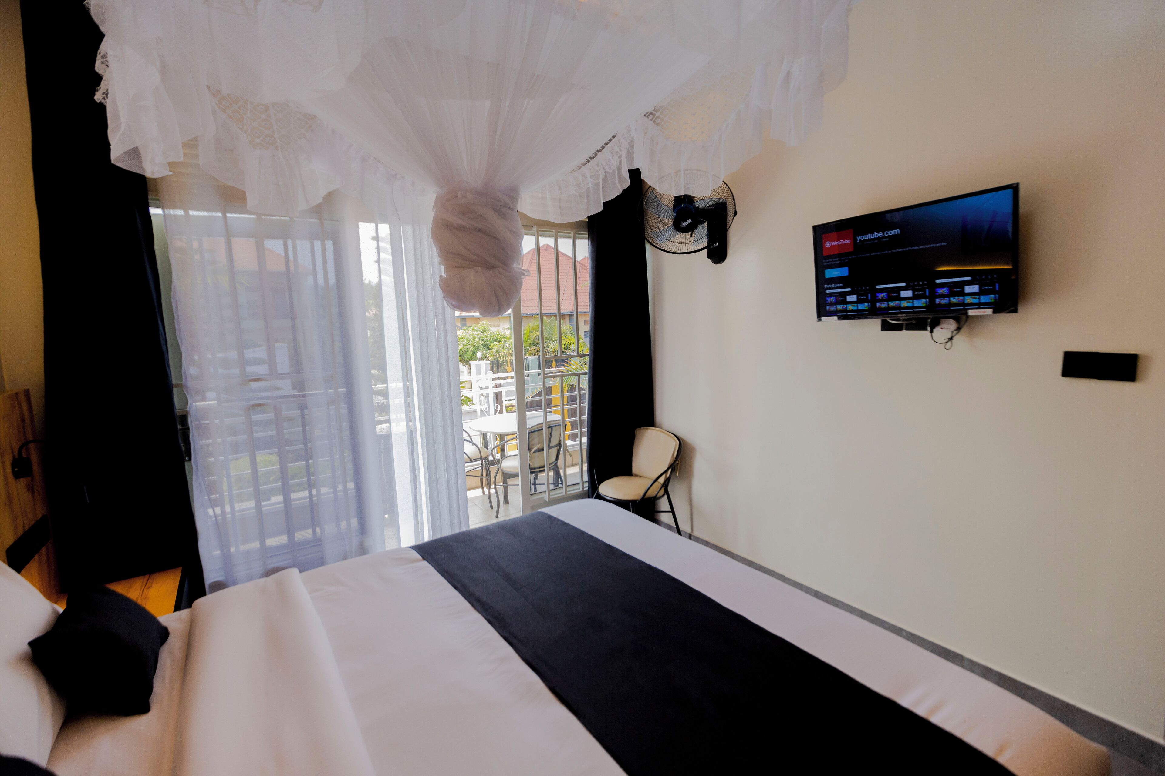 Habitación de hotel con cama, televisor montado en la pared, una silla y balcón con vistas al exterior.