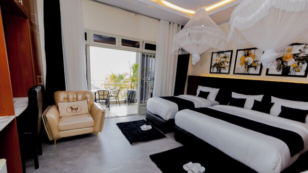 A hotel room with two beds, a sofa, a chair, a balcony with a view, and artwork on the walls.