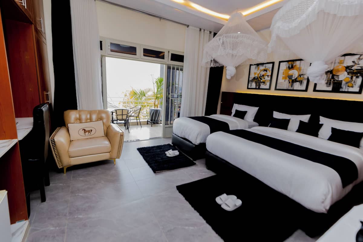 Quarto de hotel com duas camas, um sofá, uma poltrona, varanda com vista e obras de arte nas paredes.