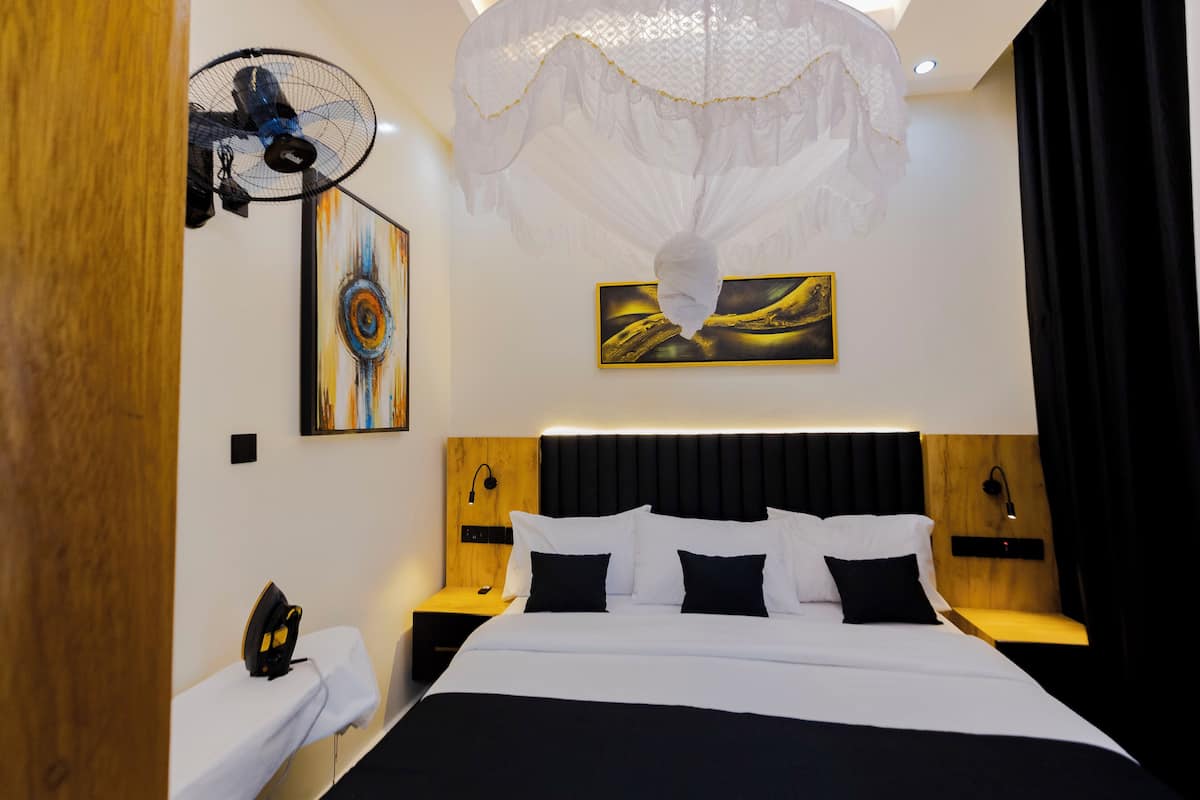 Quarto de hotel moderno com uma cama grande, cabeceira de madeira, mesas de cabeceira e obras de arte nas paredes.