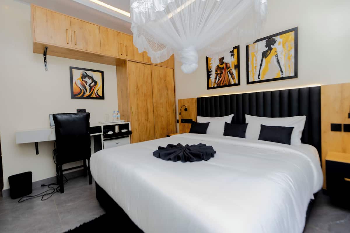 Quarto de hotel com uma cama grande, uma escrivaninha e duas pinturas na parede.