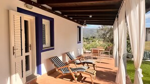 A covered patio with two lounge chairs, a table, and a view of the outdoors. - casaVerdeMare charming detached villa Sardinia (Sardegna)