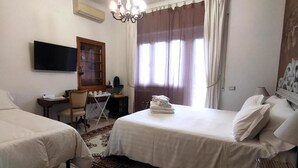 A hotel room with two beds, a desk, a chair, a television, and a chandelier.