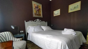 A neatly made bed with white linens, a striped armchair, and a small bedside table with a lamp.