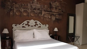 A neatly made bed with a white headboard, two bedside tables with lamps, and a large wall mural of a cityscape.