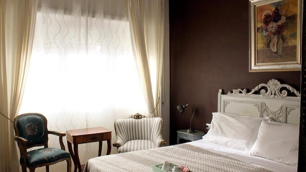 A hotel room with a bed, two chairs, a small table, and a nightstand.