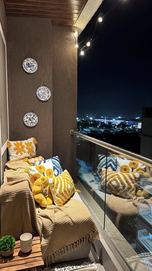 Ein Balkon mit einem Bett, dekorativen Tellern und Blick auf eine nächtliche Stadtlandschaft.