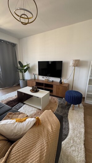 Un salon moderne avec un téléviseur à écran plat, un meuble de rangement en bois et une grande plante en pot.