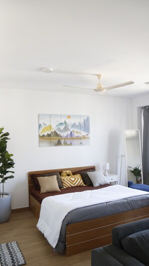 Une chambre à coucher avec un lit, un ventilateur de plafond, un tableau, une table de chevet, une lampe, une plante en pot et un lampadaire.