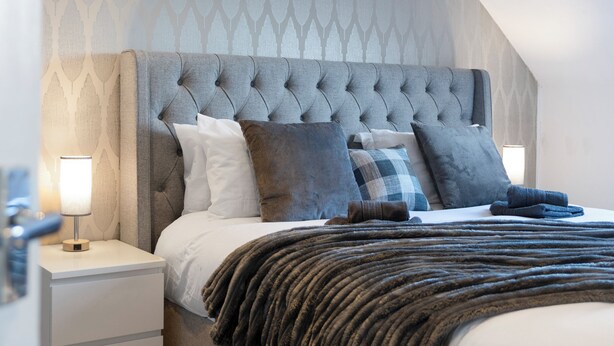 A neatly made bed with a grey upholstered headboard, white bedding, and multiple pillows.