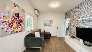 A modern living room with a grey sofa, colorful abstract art, a stone wall, and a flat-screen TV. - BEACH HOUSE BOL (Bol)