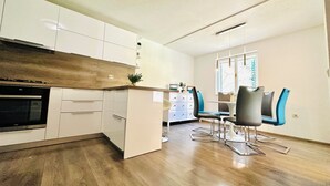A modern kitchen with white cabinets, a built-in oven, and a wooden countertop. There is a dining area with blue chairs and a table. - BEACH HOUSE BOL (Bol)